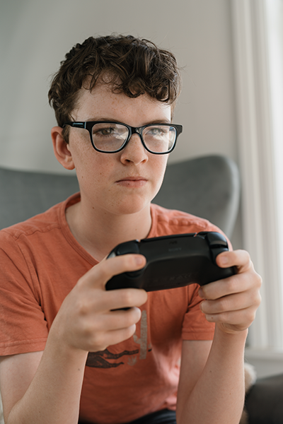 A young boy wearing glasses holds a PlayStation gaming controller